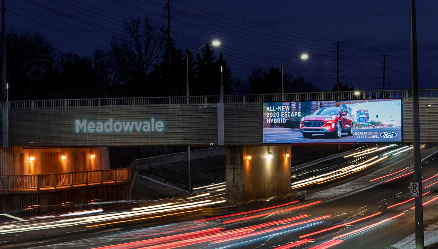 A digital billboard over a Mississauga study-route highway just after sunset, traffic streaking beneath
